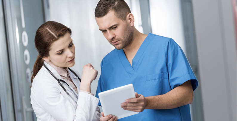 Technician and doctor looking at an electronic tablet, working together to manage disease.