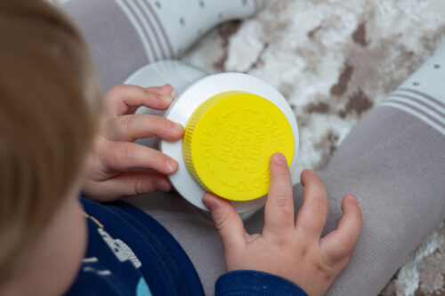 A child independently tries to open a plastic bottle of medicine with a yellow push and turn lid, close-up.