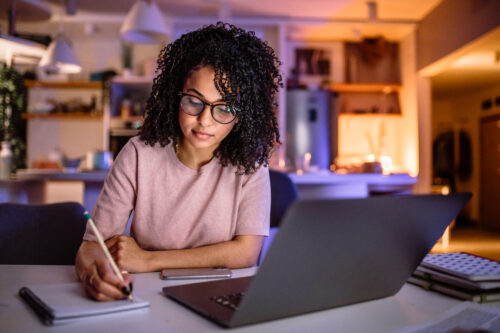 Young student girl learning for exam late at night at her home, using laptop.