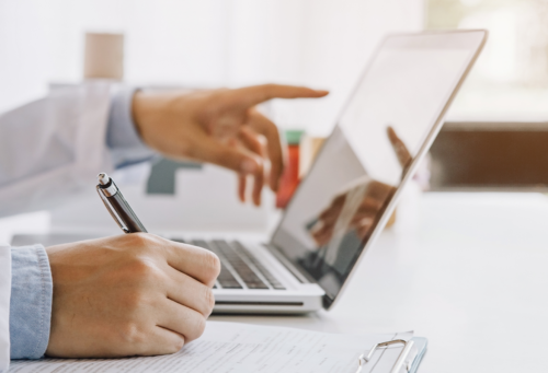 veterinarian at a laptop pointing at the screen and writing something down