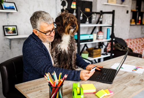 man making credit purchase on laptop while holding a dog