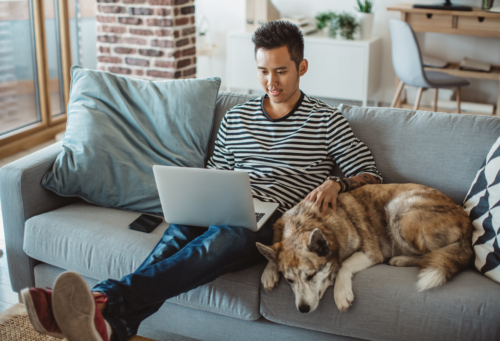 Man using computer on couch with dog