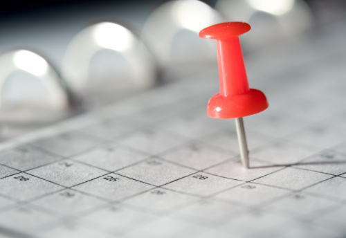 A red thumbtack pins a date on a calendar