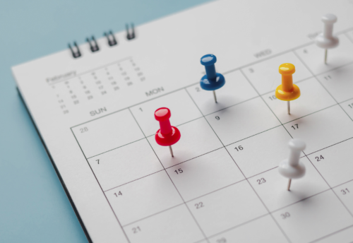 A calendar with multicolored thumbtacks on various dates.