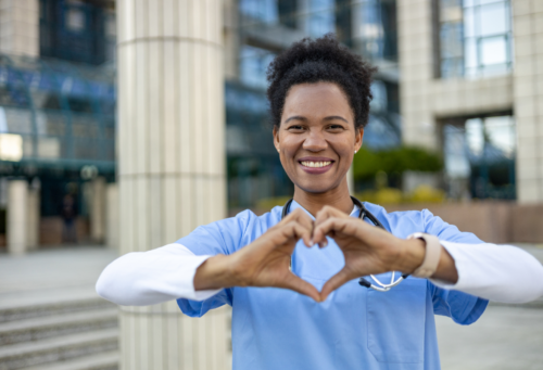 Black woman in scrubs and stethoscope makes heart with hands