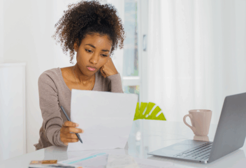 Young woman sits at a desk looking at papers and her computer with concern