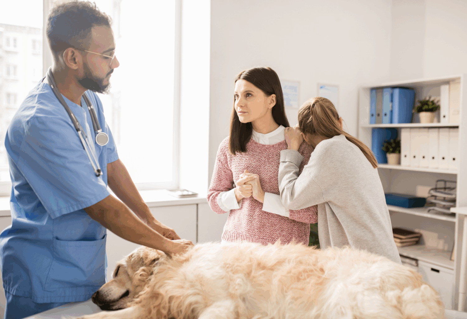 A veterinarian speaks with a female owner and her daughter while their golden retriever lies on an exam table