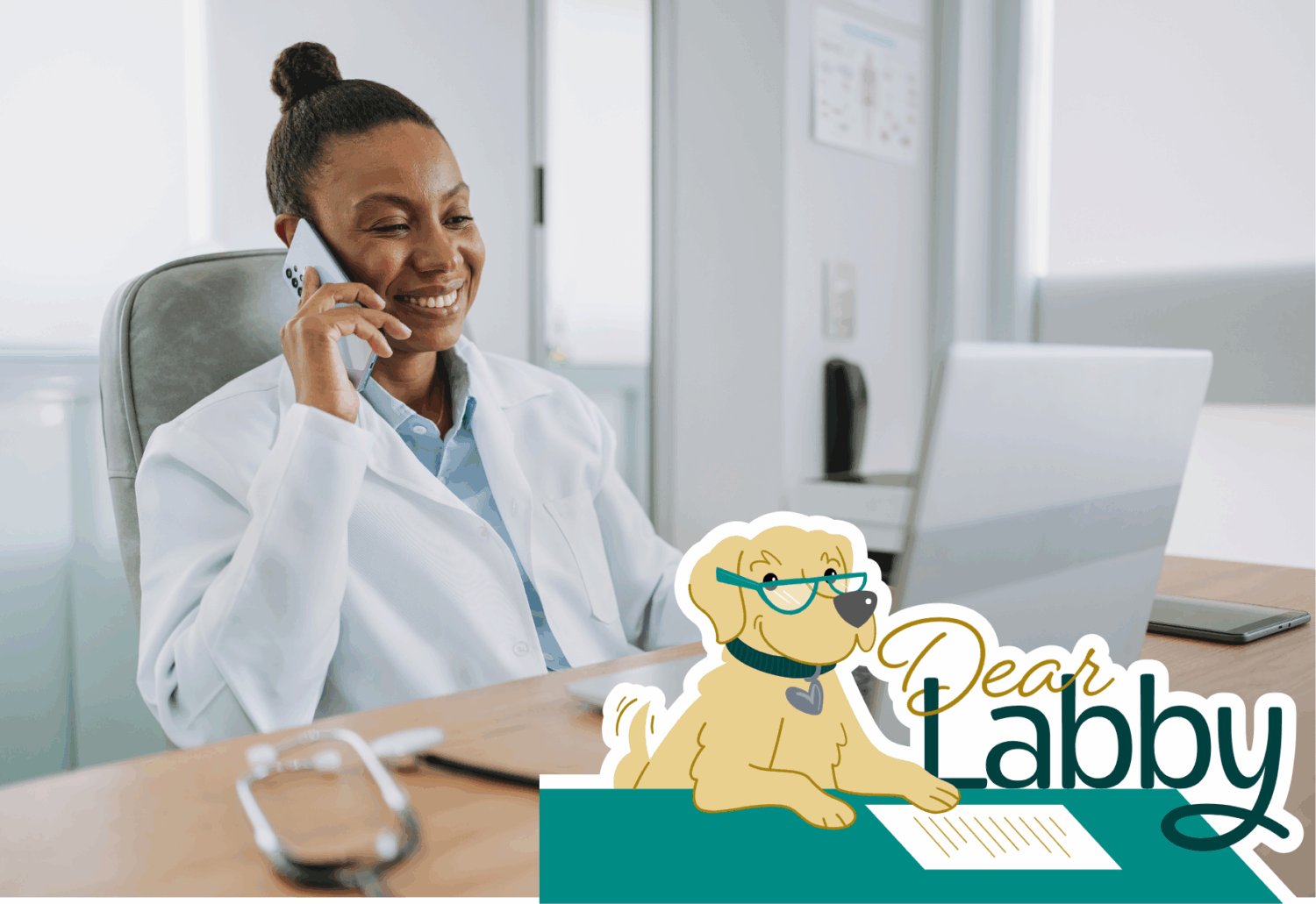 A woman in a medical coat sits behind a laptop talking on the phone and smiling