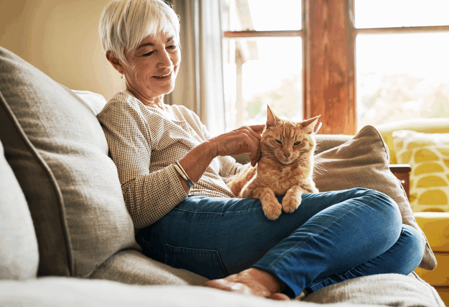 An elderly woman sitting on her couch with an orange cat on her lap