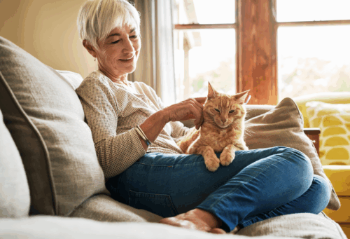 An elderly woman sitting on her couch with an orange cat on her lap
