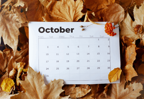 An October calendar sits atop a backdrop of fall leaves
