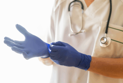 healthcare professional wearing scrubs and a stethoscope putting on blue nitrile gloves