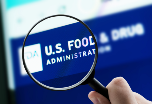 A hand holding a magnifying glass in front of the FDA website
