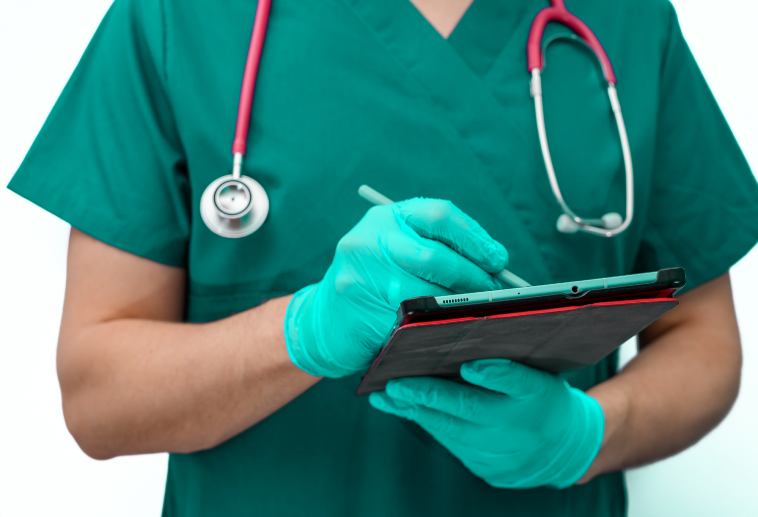 A person wearing scrubs and a stethoscope and exam gloves holding a tablet and writing on it with a stylus