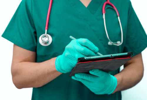 A person wearing scrubs and a stethoscope and exam gloves holding a tablet and writing on it with a stylus