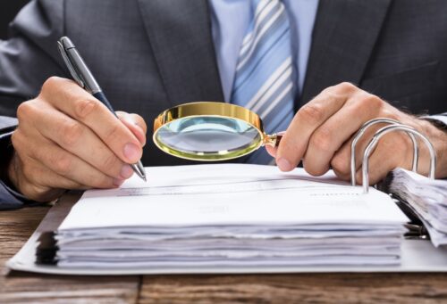 Midsection of businessman examining invoice with magnifying glass at desk