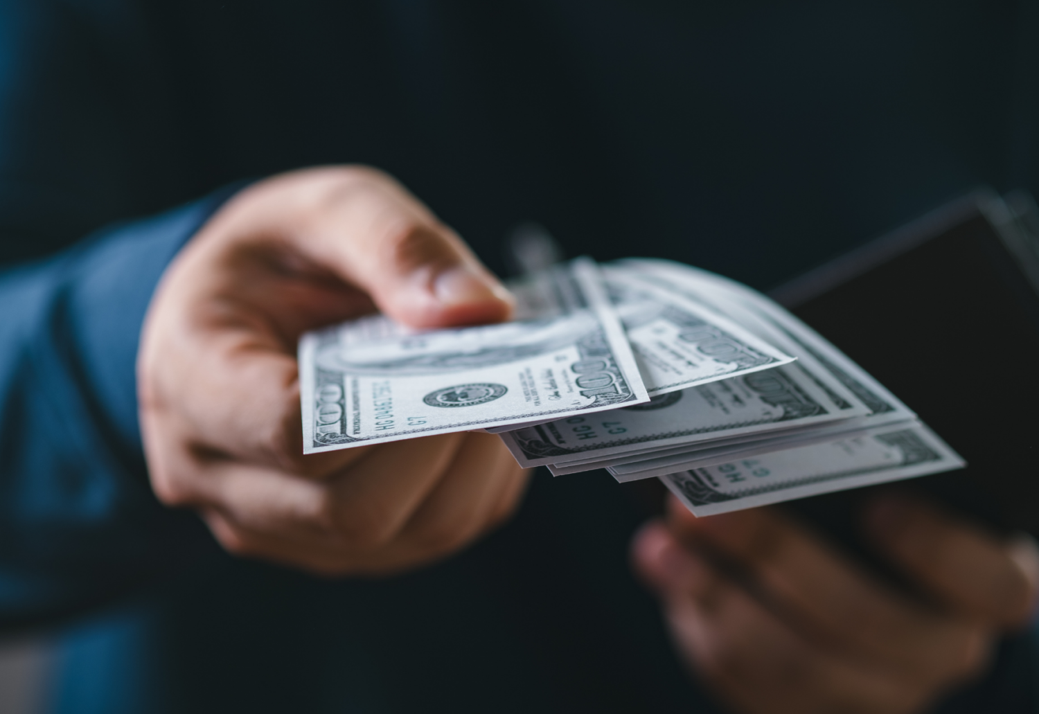 A man is handing out multiple hundred dollar bills.