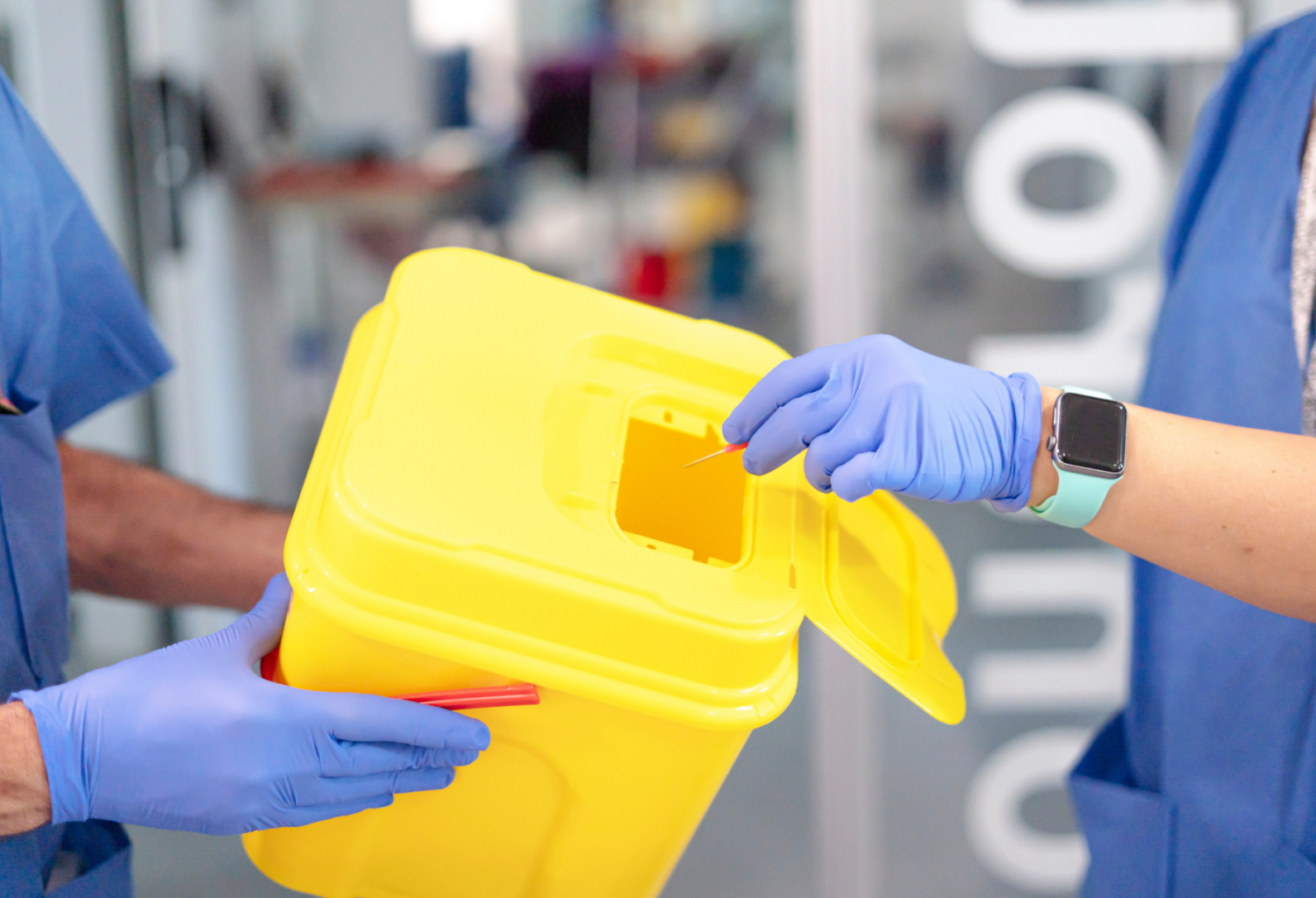 A team member discarding a used IV catheter in a yellow hard plastic container held by another team member.